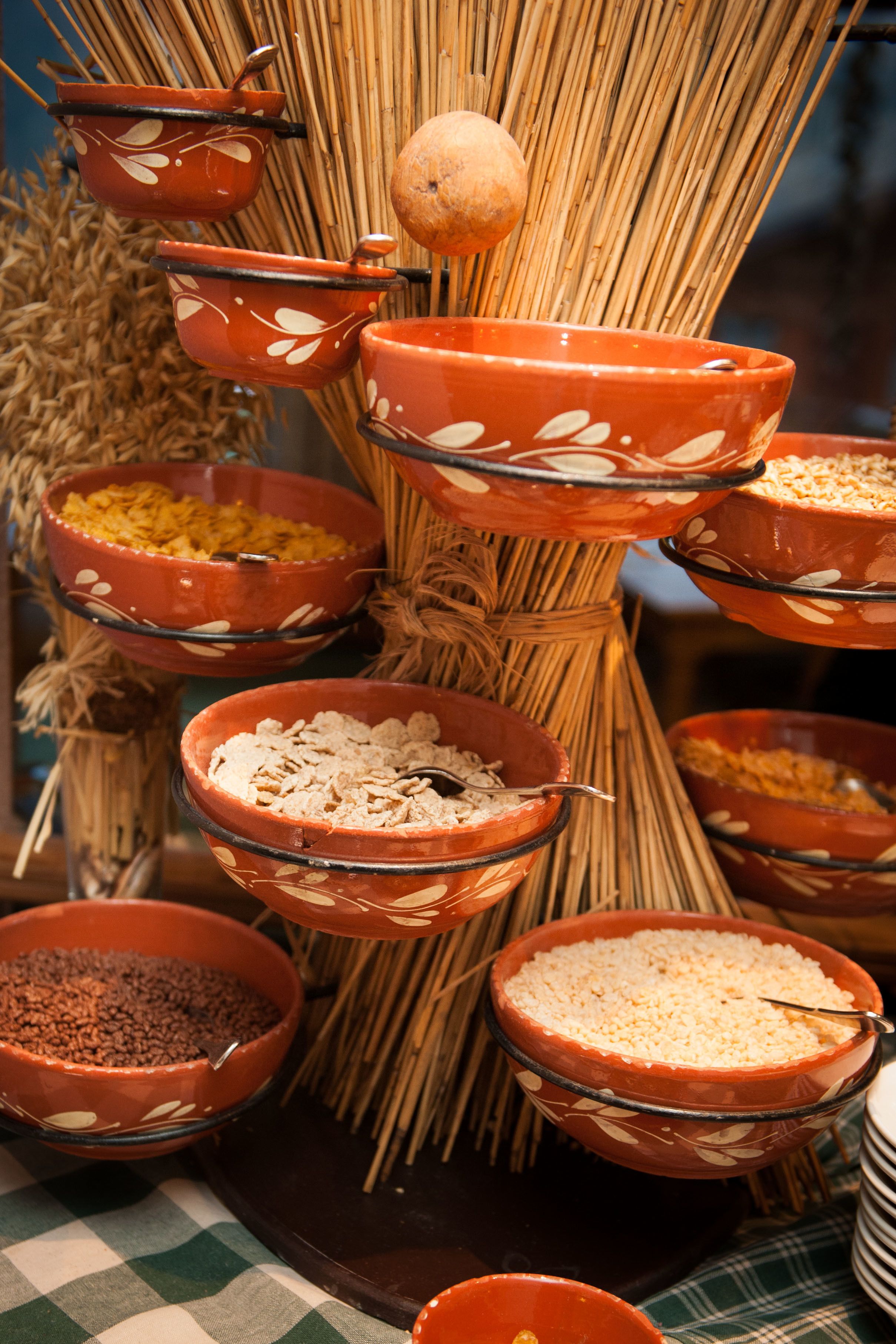 A tiered display of terracotta bowls with various grains and seeds, arranged on a woven structure.