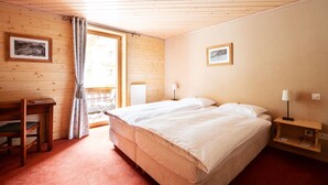 A bedroom with a bed, a desk, a chair, a window with curtains, and two framed pictures on the walls. - Hotel Suisse (Champery)