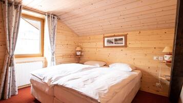 Um quarto de madeira com uma cama, uma janela com cortinas, um quadro na parede e uma mesa de cabeceira com abajur.