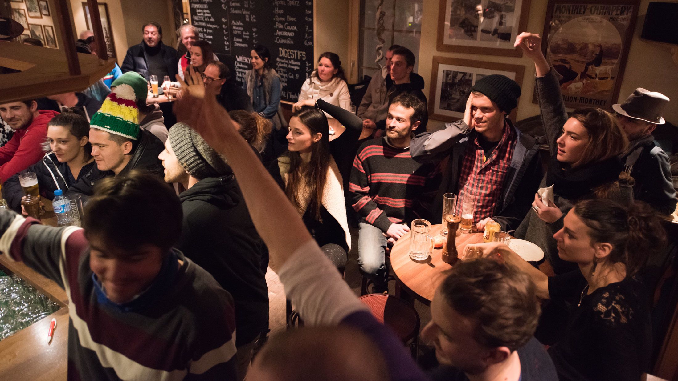 Un groupe de personnes s’est réuni autour d’une table dans un endroit peu éclairé, vraisemblablement un bar ou un restaurant, et un menu était affiché sur le mur.