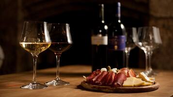 Dos copas de vino con una botella, un plato de embutidos y queso sobre una mesa de madera.