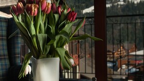A table with a vase of tulips, a cup of tea, and a pastry on a balcony with a mountain view. - Hotel Suisse (Champery)