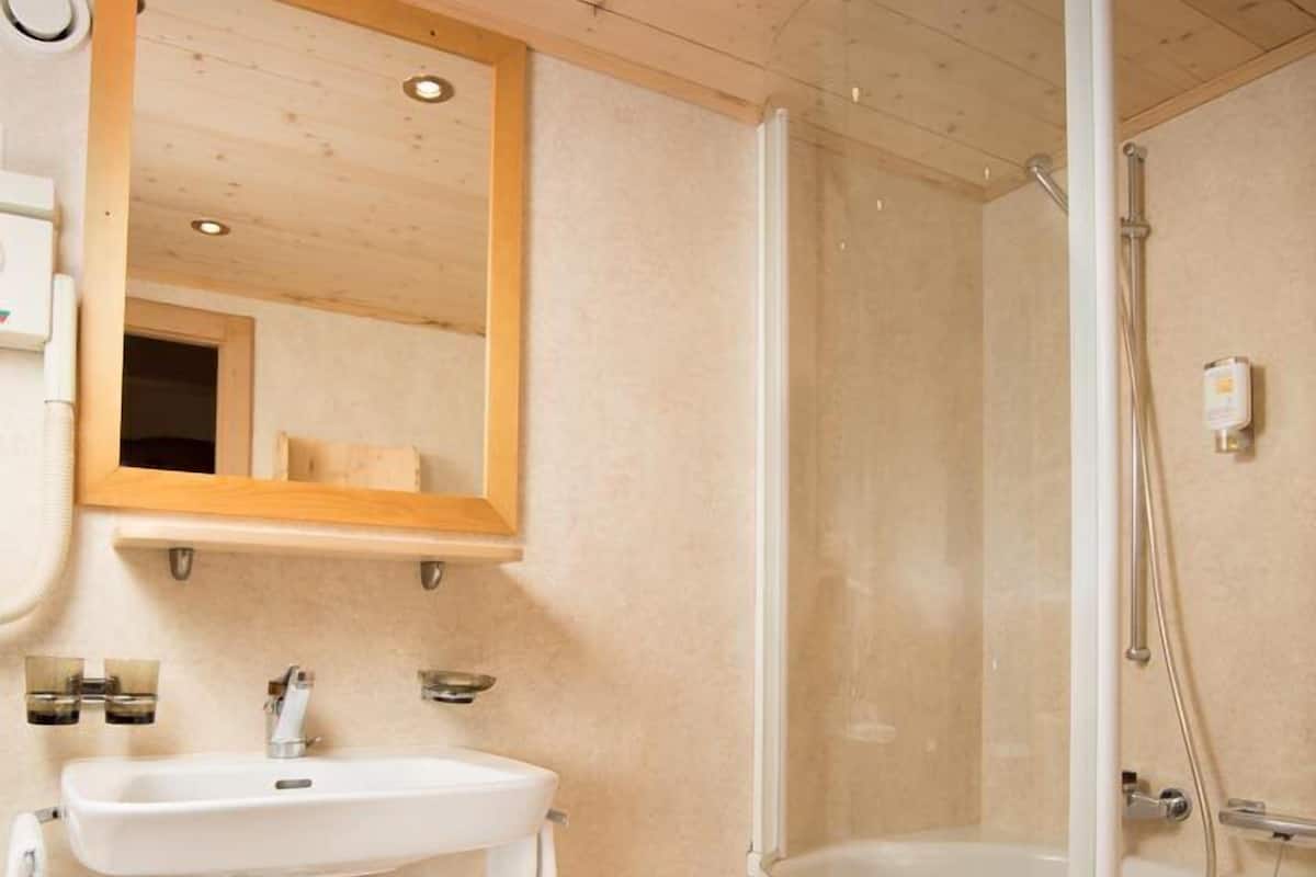 A bathroom with a sink, mirror, shower, and a trash bin.