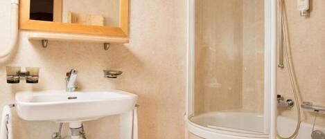 A bathroom with a sink, mirror, shower, and a trash bin.