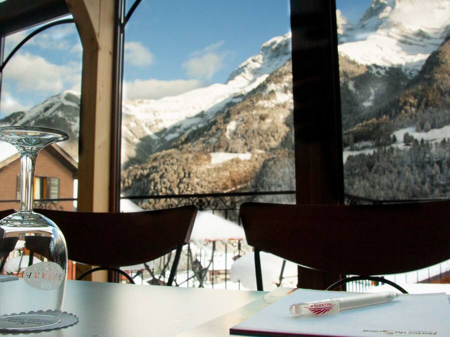 Una mesa con una copa de cristal, un cuaderno y un bolígrafo, con vistas a un paisaje montañoso a través de amplios ventanales.