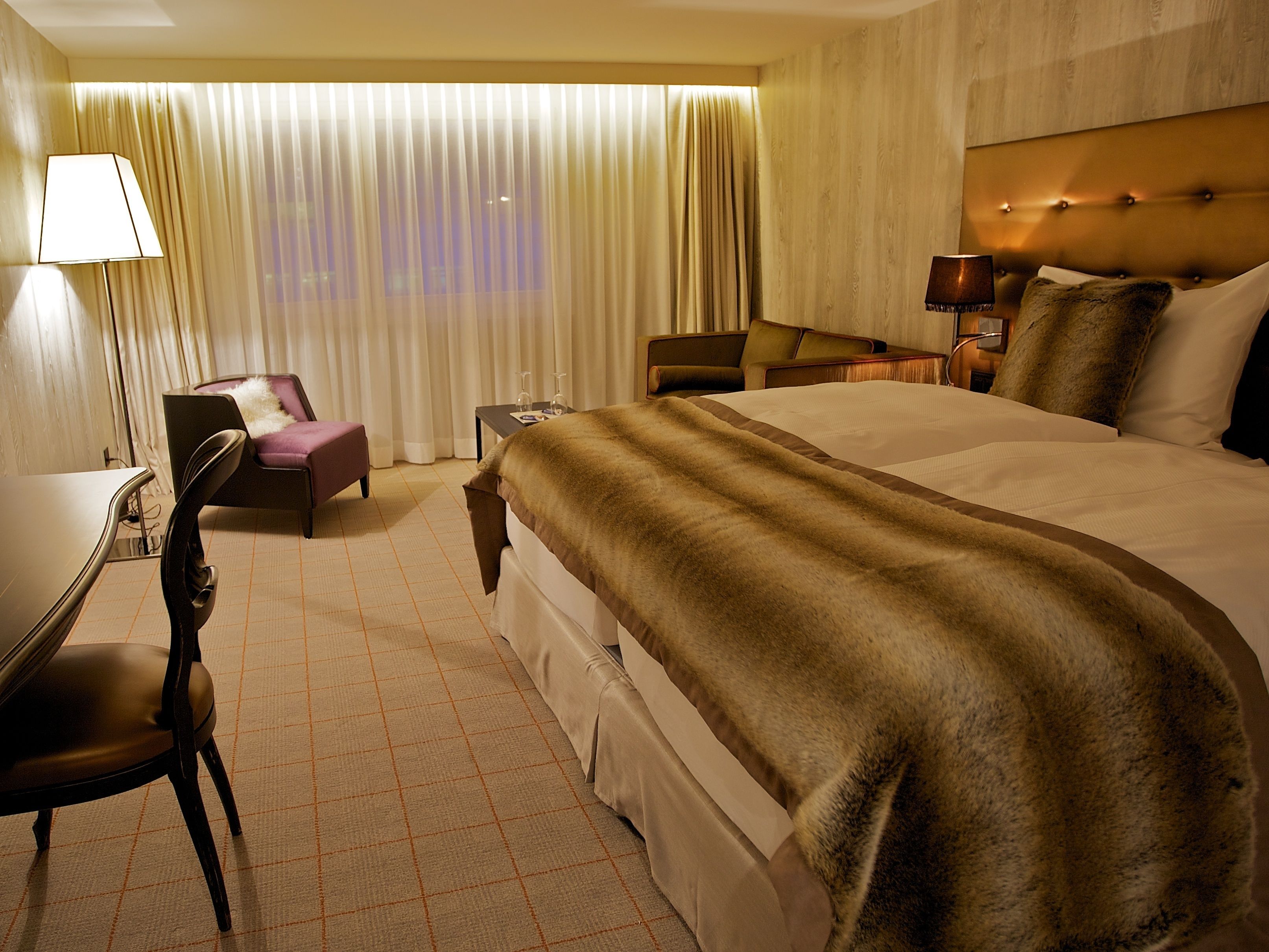 Una habitación de hotel con una cama grande, un escritorio, una silla y una mesita con una lámpara.