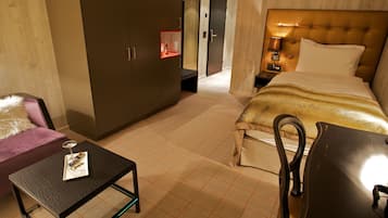 Una habitación de hotel con cama, escritorio, silla, armario y mesita de noche con lámpara.
