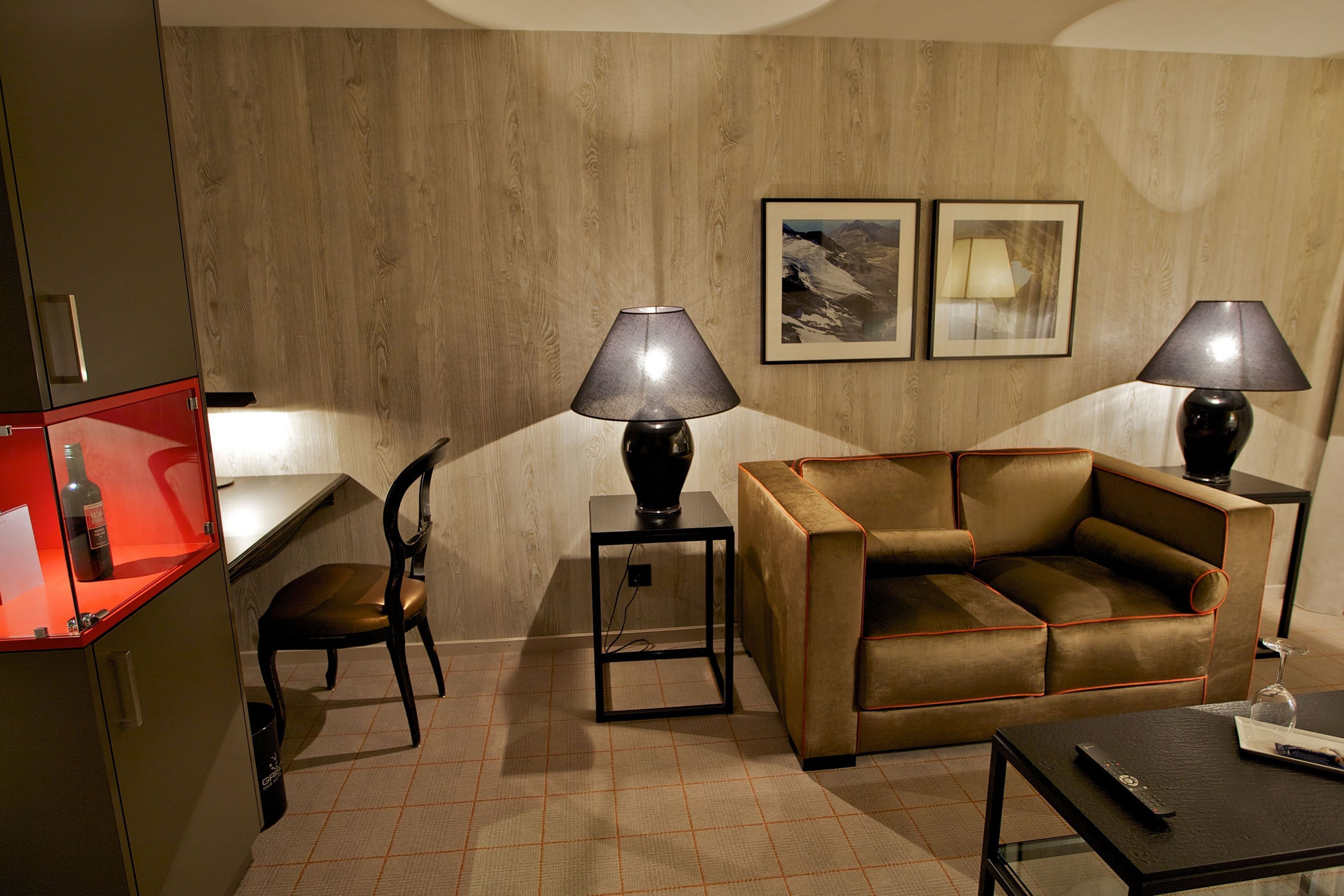 Una habitación con un sofá de cuero marrón, dos lámparas negras, una pared de madera, una mesita pequeña y una silla.