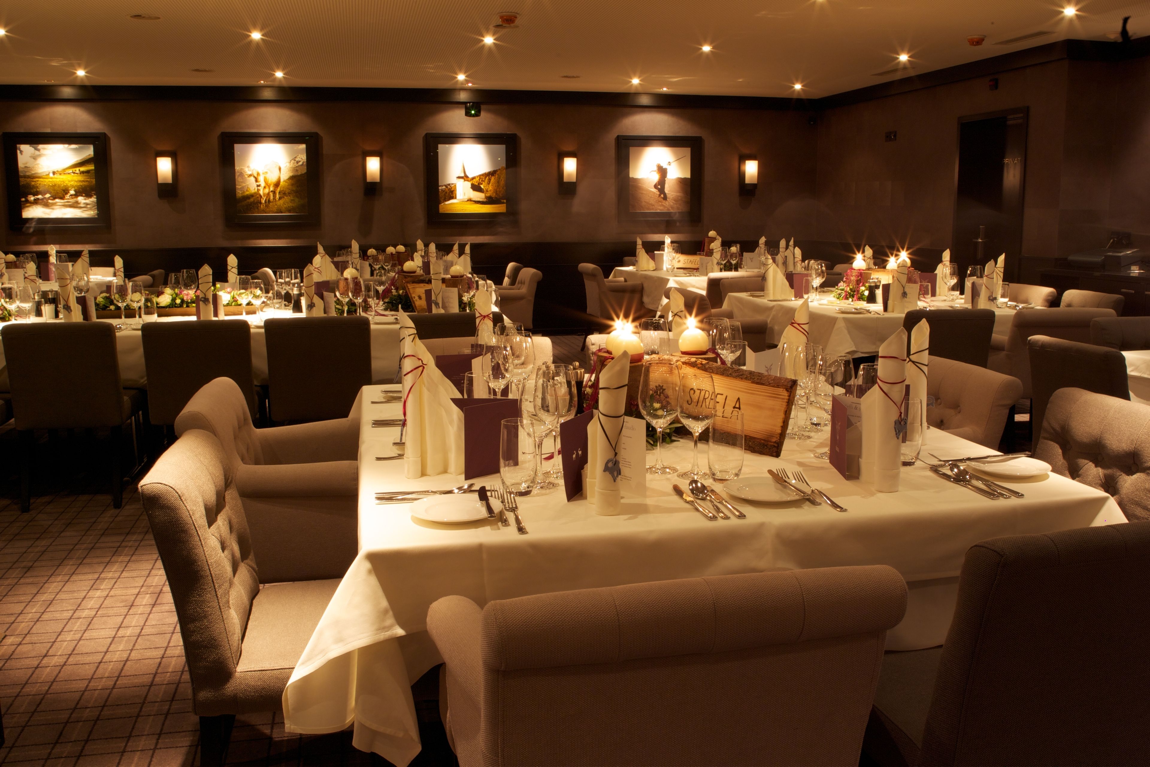 Un restaurante con varias mesas dispuestas para comer, cada una con mantel blanco, velas y cubertería impecable.