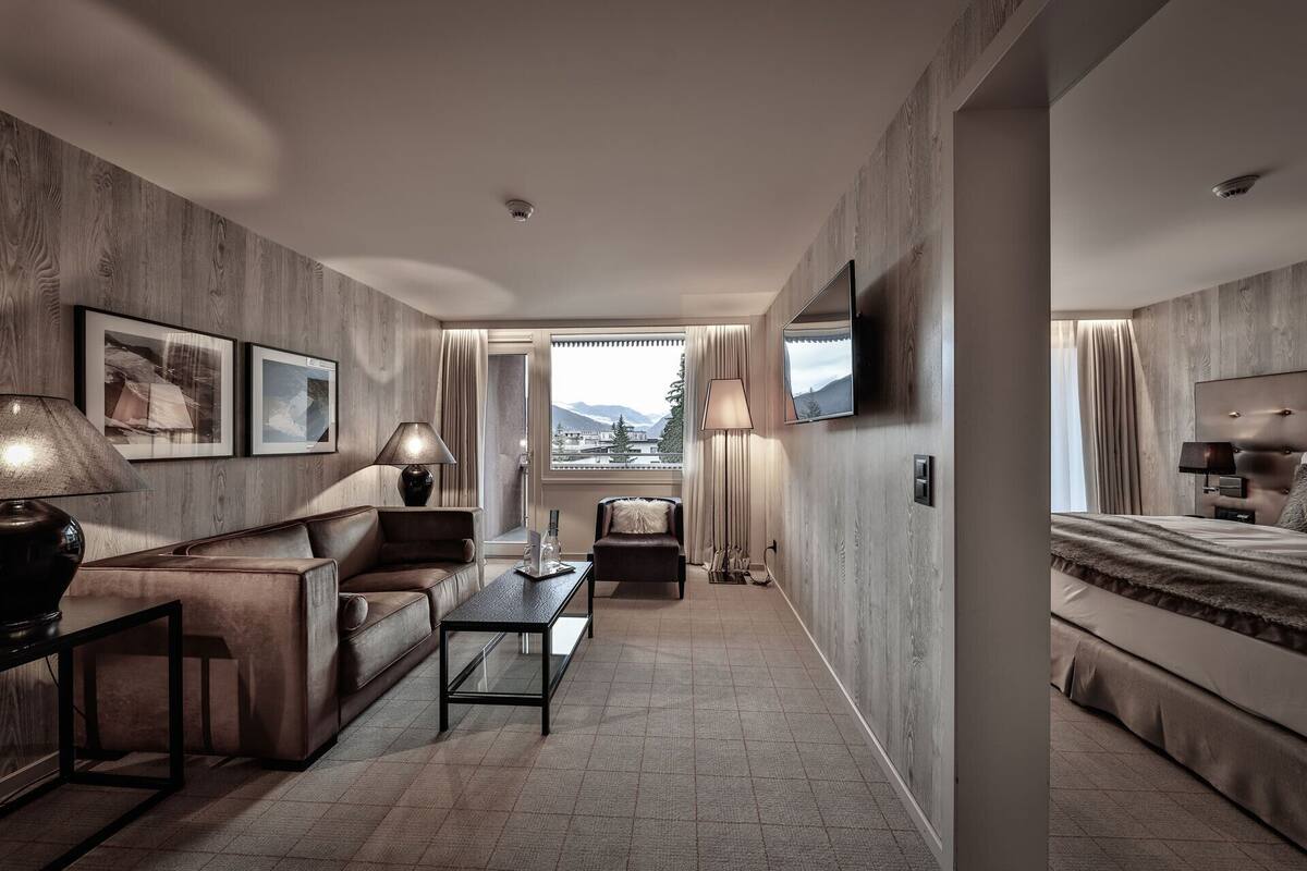 A hotel room with a sofa, armchair, coffee table, TV, and a bed.