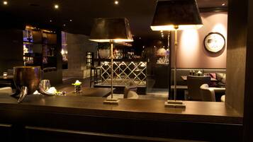 A bar area with a counter, two lamps, a clock, and a seating area with chairs.