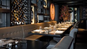 Un restaurante moderno con una larga mesa de comedor, cabinas acolchadas y una pared decorativa con patrones geométricos.