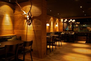 A restaurant with wooden walls, a deer head mounted on the wall, and tables with chairs. - Grischa - DAS Hotel Davos (Davos)