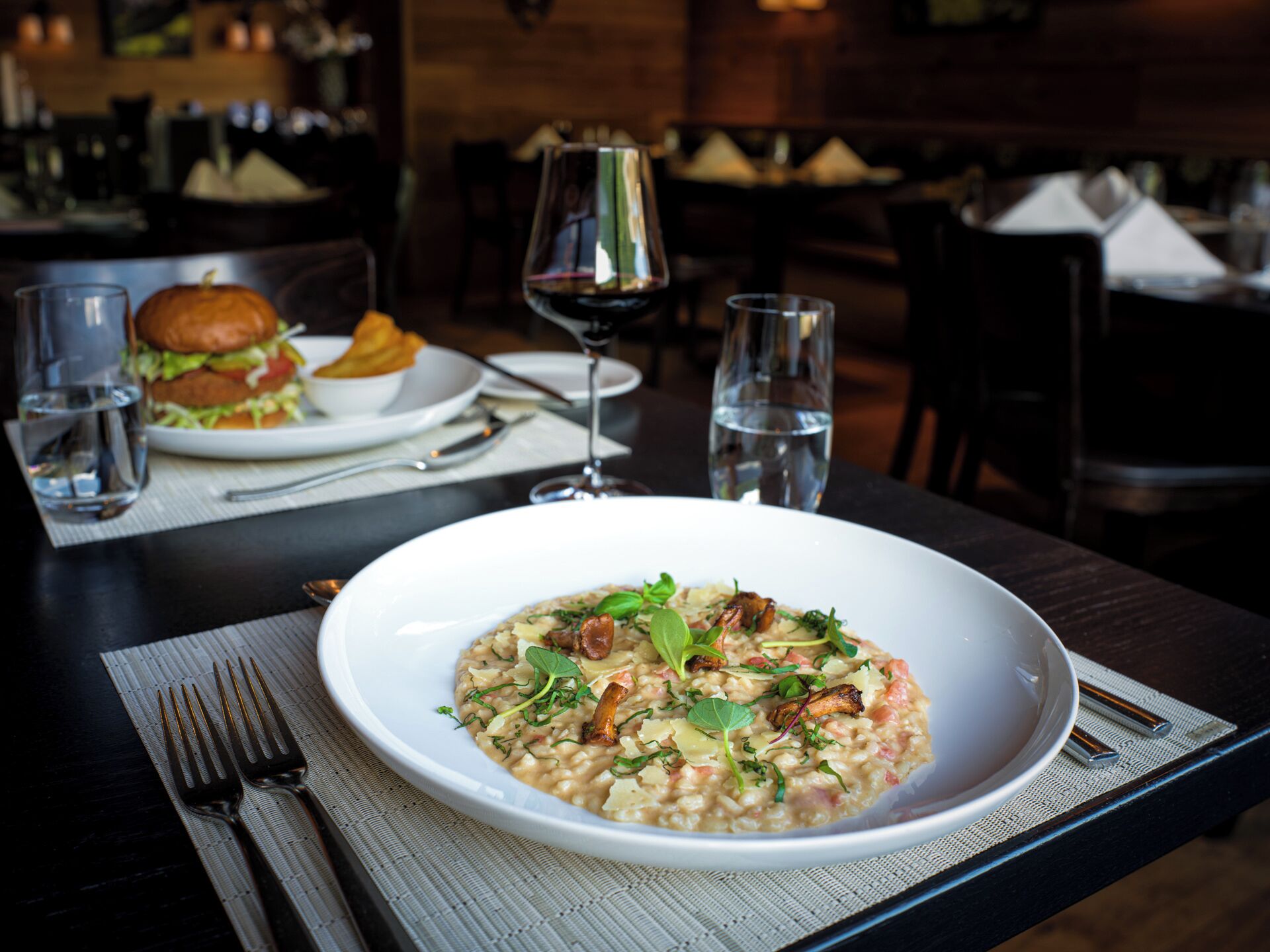 Una mesa con un plato de risotto, una copa de vino y una hamburguesa al fondo.