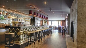 Una zona de bar con una barra larga, varios taburetes y una amplia variedad de botellas y vasos.