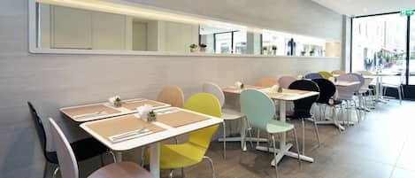A modern dining area with multiple tables and chairs, a long mirror, and a view of the street outside.