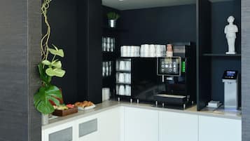 Una cuina moderna amb armaris blancs, una màquina de cafè i una petita planta.