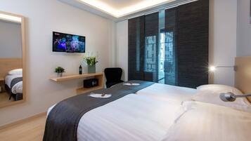 Una habitación de hotel moderna con una cama grande, un televisor montado en la pared, un pequeño escritorio con una planta y una ventana con vista a la ciudad.