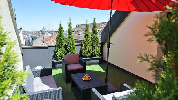 Une terrasse sur le toit, aménagée avec du mobilier d’extérieur, un parasol rouge et des plantes en pot.