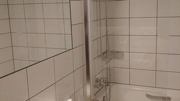 Un baño con azulejos blancos, una bañera, una ducha con puerta de vidrio y un inodoro.