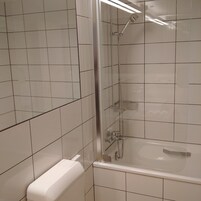 Un baño con azulejos blancos, una bañera, una ducha con puerta de vidrio y un inodoro.