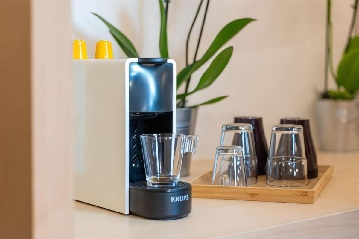 Una cafetera con depósito de agua, una jarra de café y cuatro tazas sobre una bandeja.