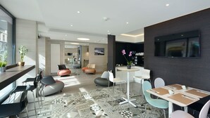 Un hall d’hôtel moderne doté d’un bar, de différents espaces de détente et d’un grand écran de télévision.