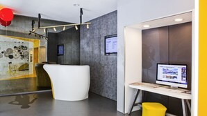 Un espai d'oficina modern amb un taulell de recepció blanc corbat, un ordinador sobre un escriptori blanc i un tamboret groc.