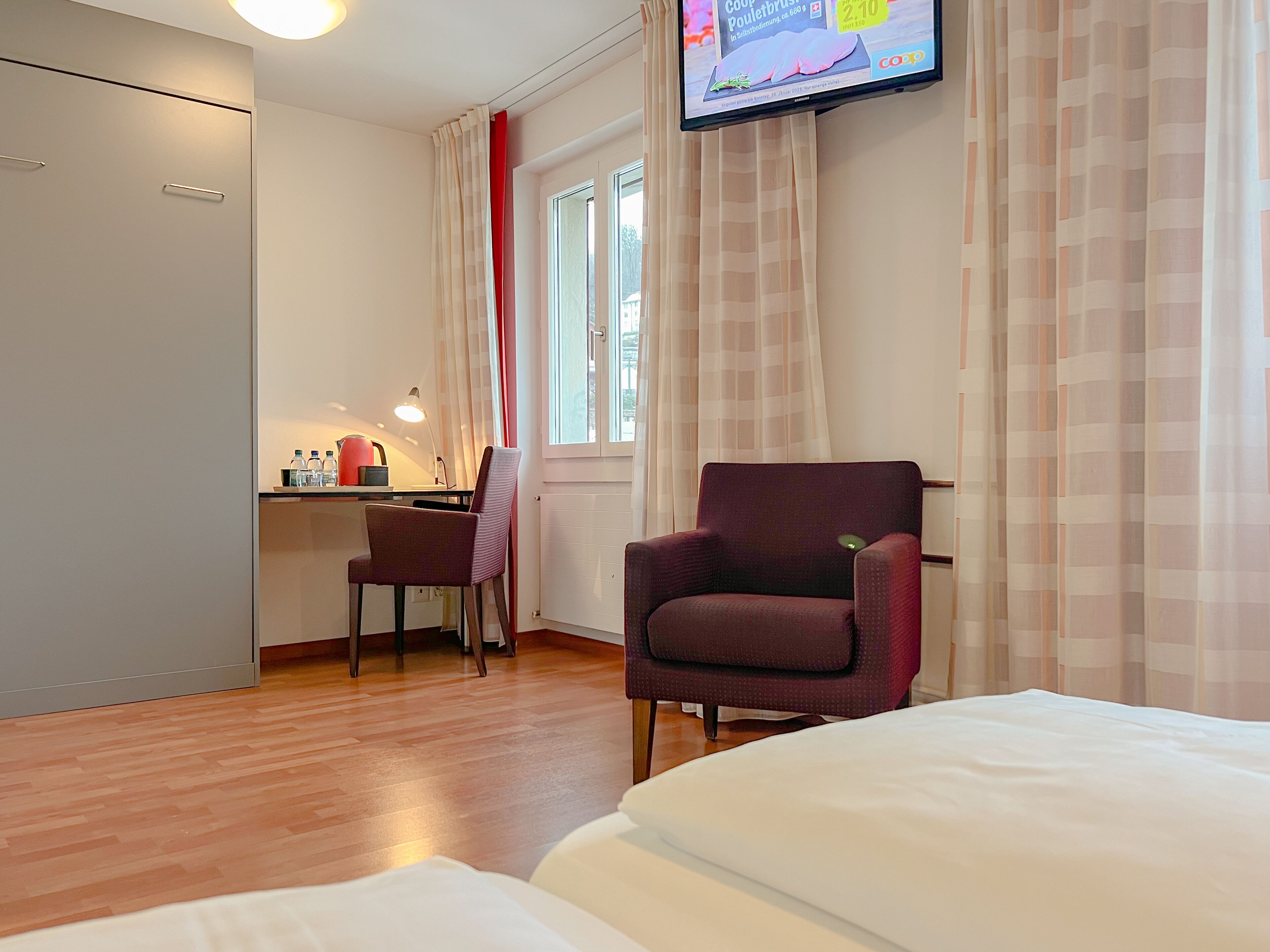 A hotel room with a bed, a desk, a chair, and a television.