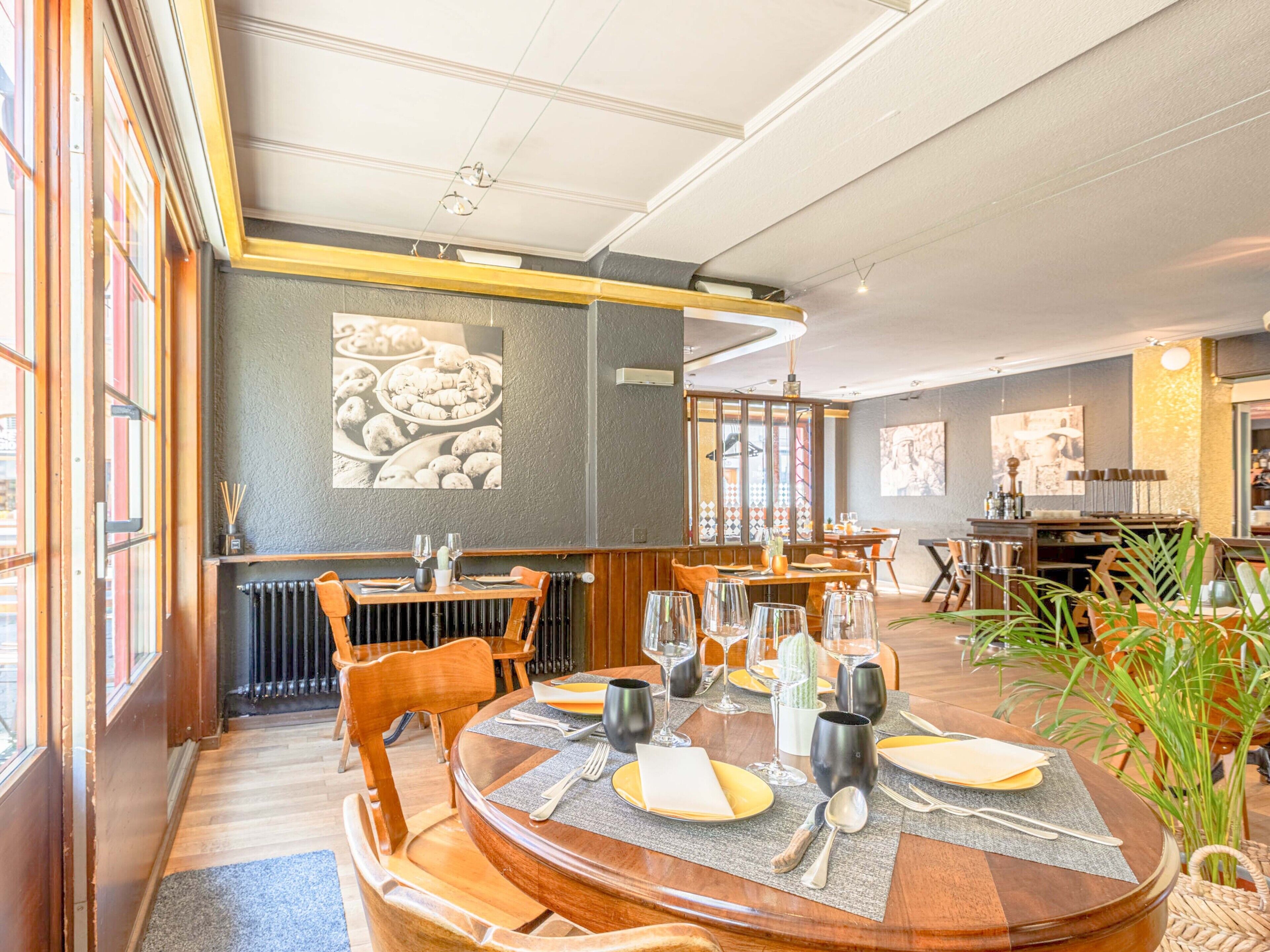 Ein Restaurant mit runden Tischen, einem großen Fenster links und einer Wand mit einem Foto von Speisen.