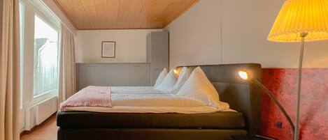 A bedroom with a bed, bedside table, lamp, and a window with curtains.