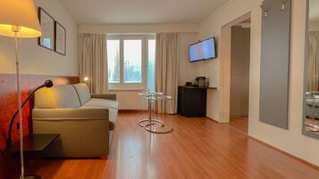 A modern hotel room with a sofa, a small table, a TV, and a mirror.