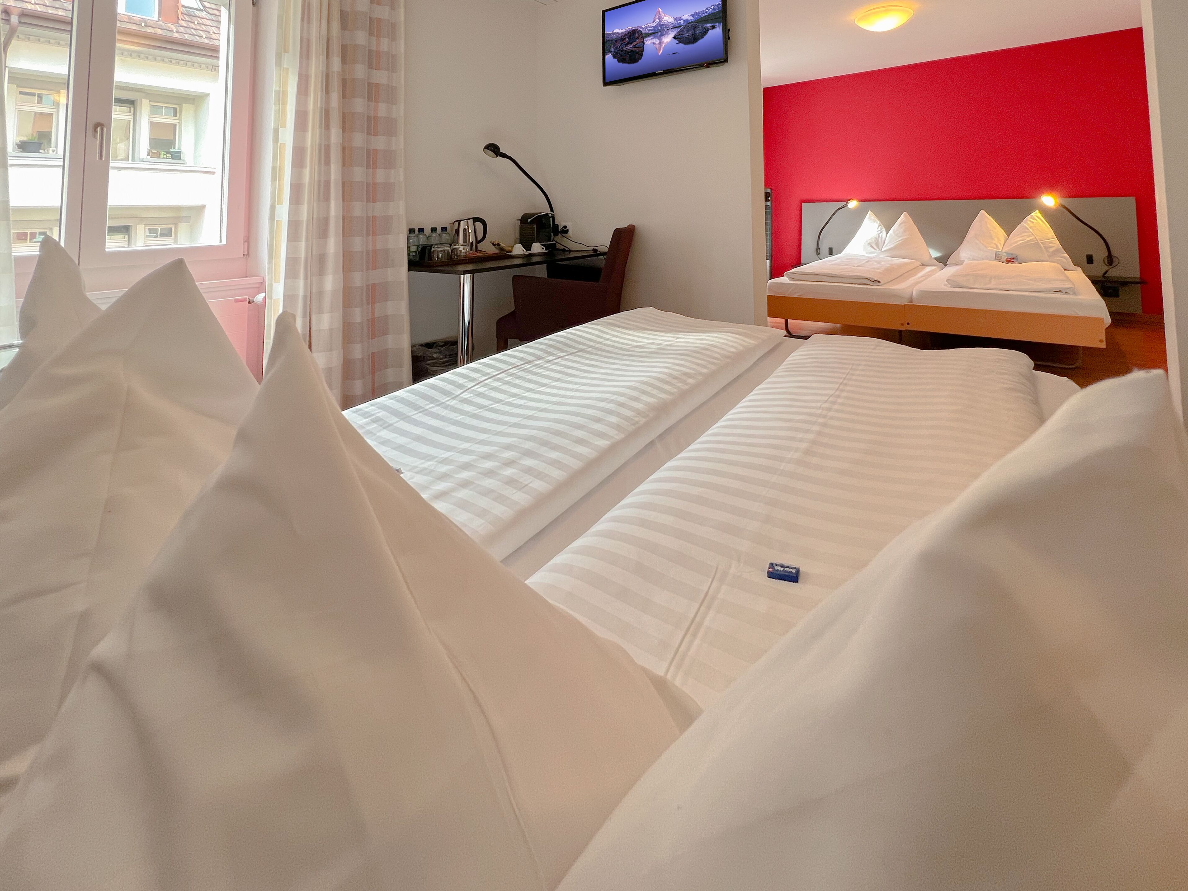 Habitació d'hotel amb llit, escriptori, cadira, televisió i una paret vermella decorativa.