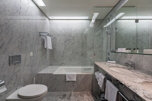 Un baño moderno con piso de mármol, una bañera, un lavamanos y un inodoro.