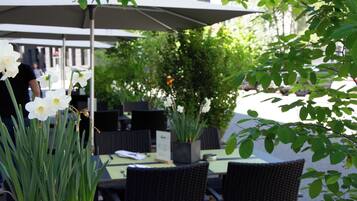 An outdoor seating area with tables and chairs, a covered umbrella, and a potted plant.