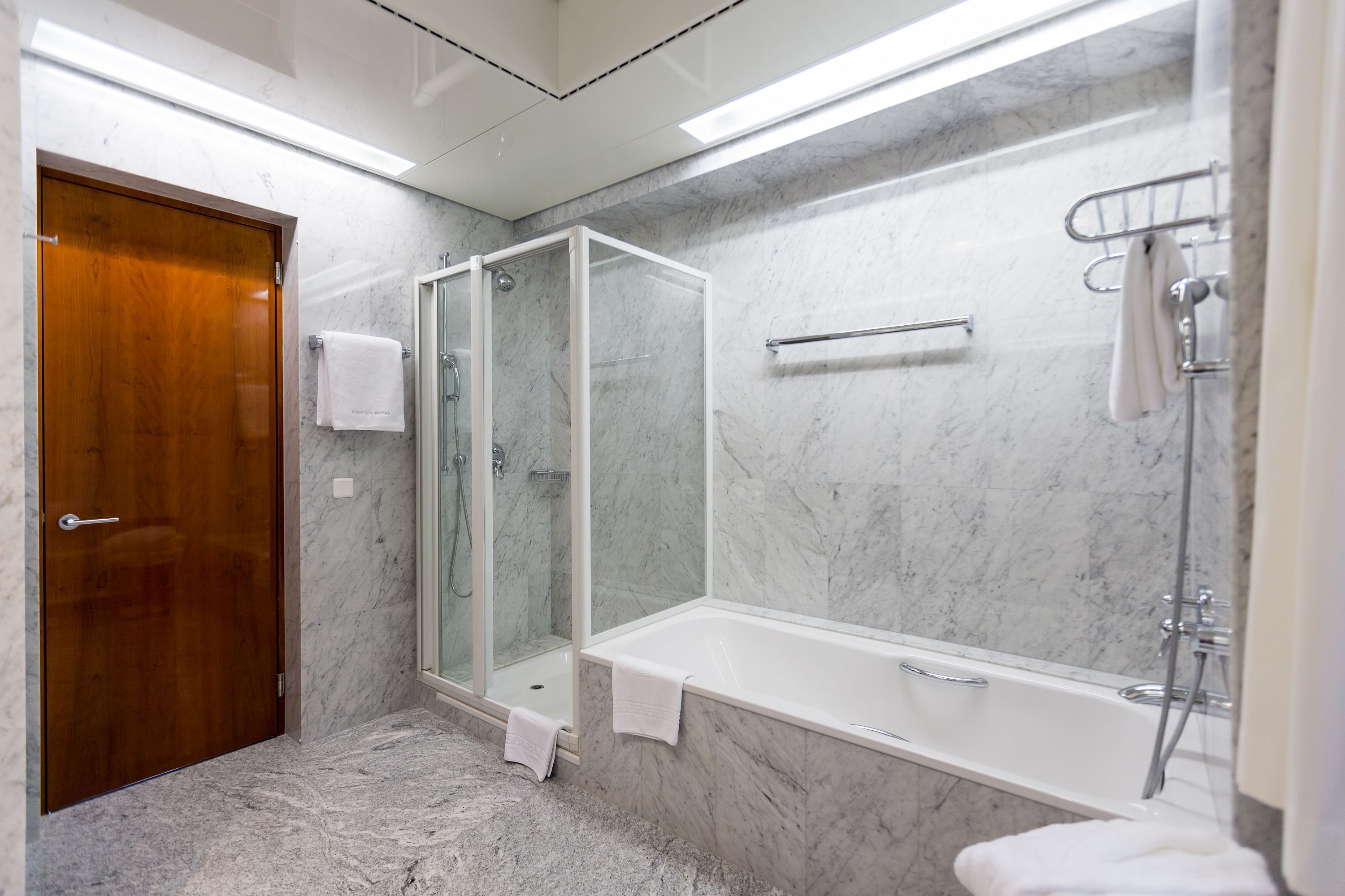 Ein modernes Badezimmer mit Marmorboden, einer gläsernen Duschkabine, einer weißen Badewanne und einer Holztür.