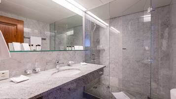 Une salle de bain moderne avec un comptoir en marbre, deux vasques, une douche à l’italienne en verre et un grand miroir.