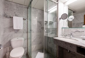Un baño moderno con ducha de vidrio, pared de azulejos de mármol, inodoro blanco y lavamanos con encimera de granito.