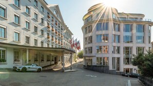 A hotel with a classical facade, a modern wing, and a white car parked in front.
