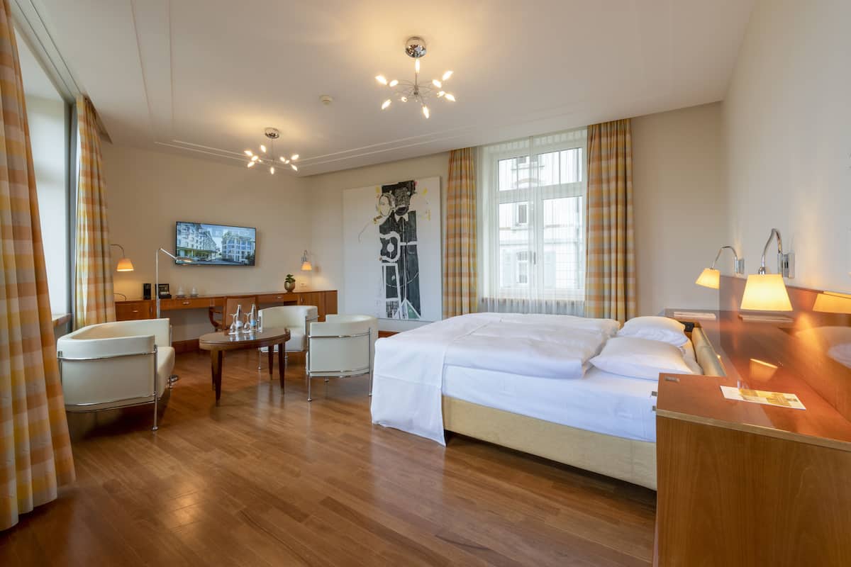A hotel room with a large bed, a desk, a chair, a TV, and a window with curtains.