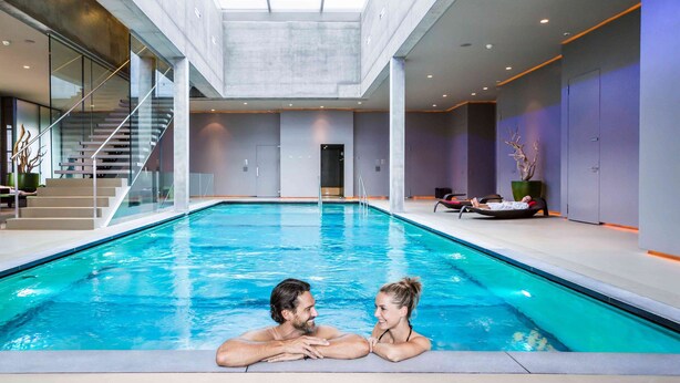An indoor swimming pool with a glass-enclosed staircase and a view of the sky through the ceiling.