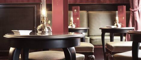 A room with a round table, two chairs, a mirror, a chandelier, and a wall-mounted lamp.