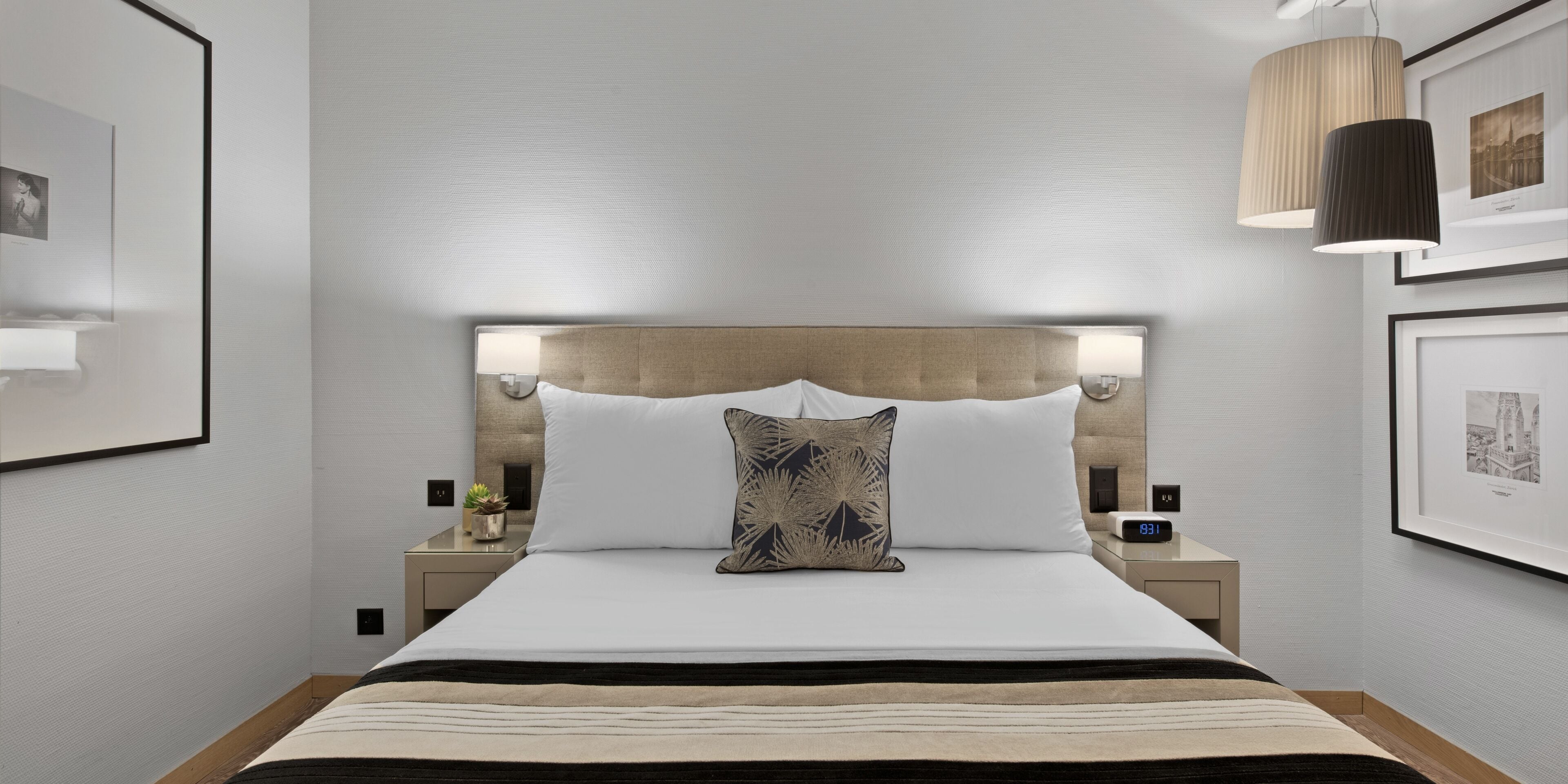 Une chambre d’hôtel moderne dotée d’un grand lit, d’une tête de lit avec éclairage intégré, de tables de chevet avec lampes et de tableaux encadrés aux murs.