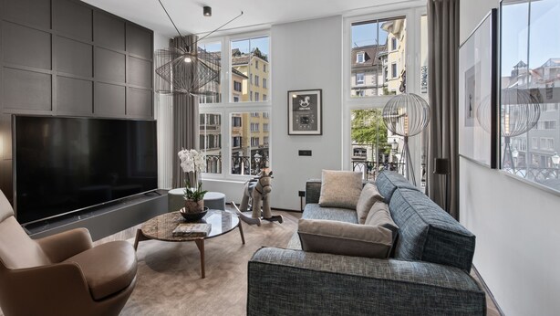 Una sala de estar moderna con un televisor de pantalla plana grande, asientos cómodos y amplios ventanales con vistas a la ciudad.