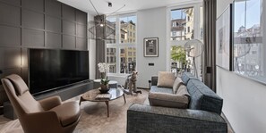 Una sala de estar moderna con un televisor de pantalla plana grande, asientos cómodos y amplios ventanales con vistas a la ciudad.