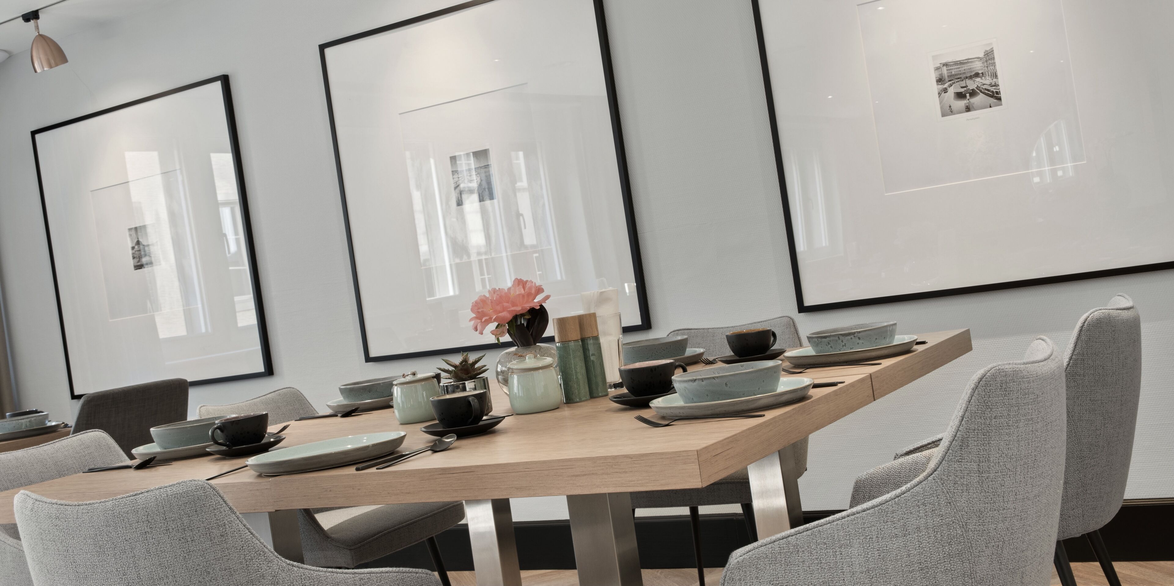 Un comedor moderno con una mesa de madera, sillas tapizadas de gris y obras de arte enmarcadas en las paredes.