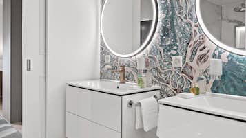 Une salle de bain moderne avec un meuble-lavabo blanc, un miroir rond et un mur décoré d’un motif imitant le marbre.