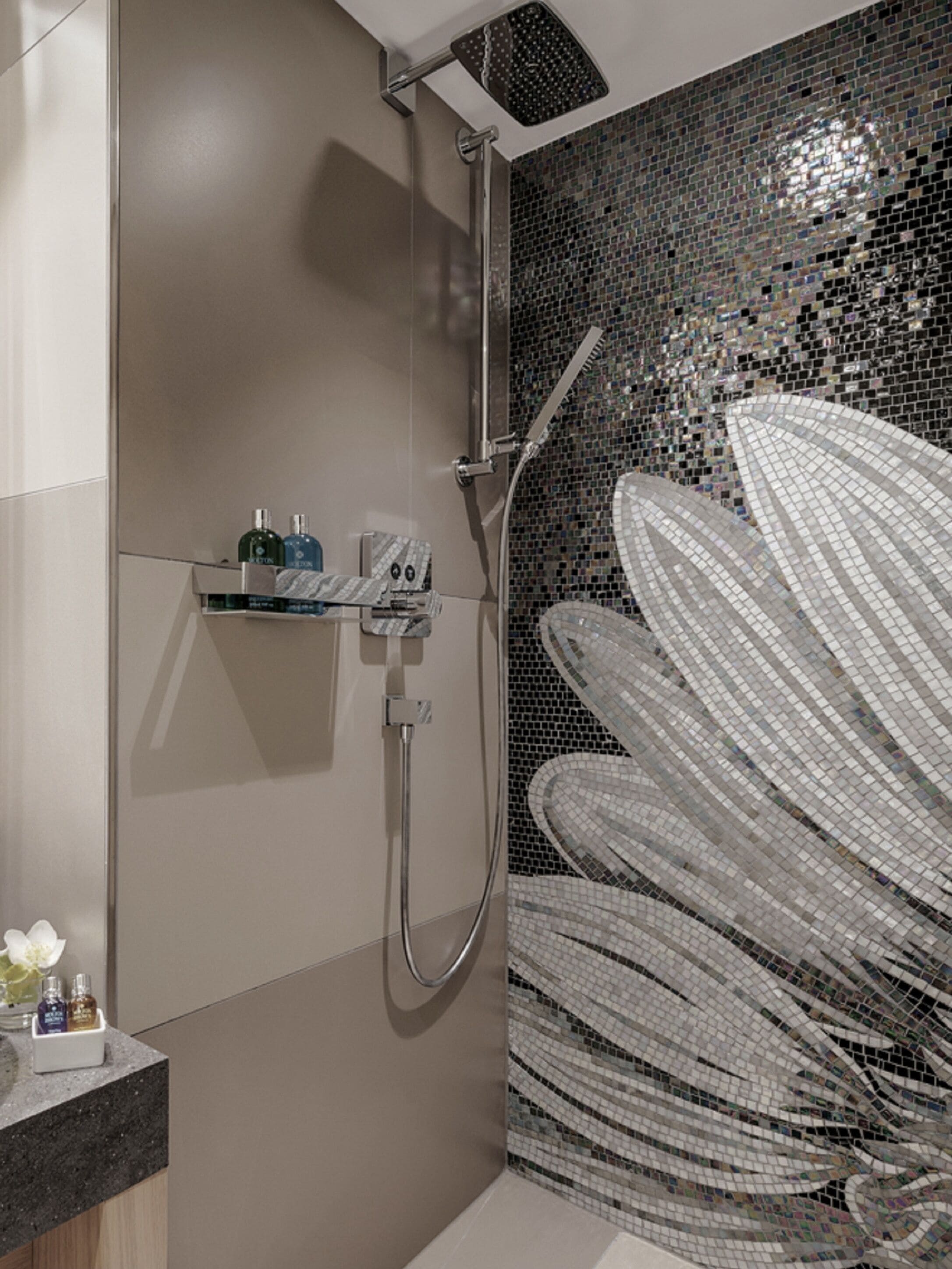 Et moderne badeværelse med bruser, flisebeklædt væg og et hyldesæt med toiletartikler.