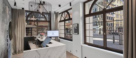 A modern reception desk with a marble top, large windows offering a view of the street, and a contemporary chandelier.