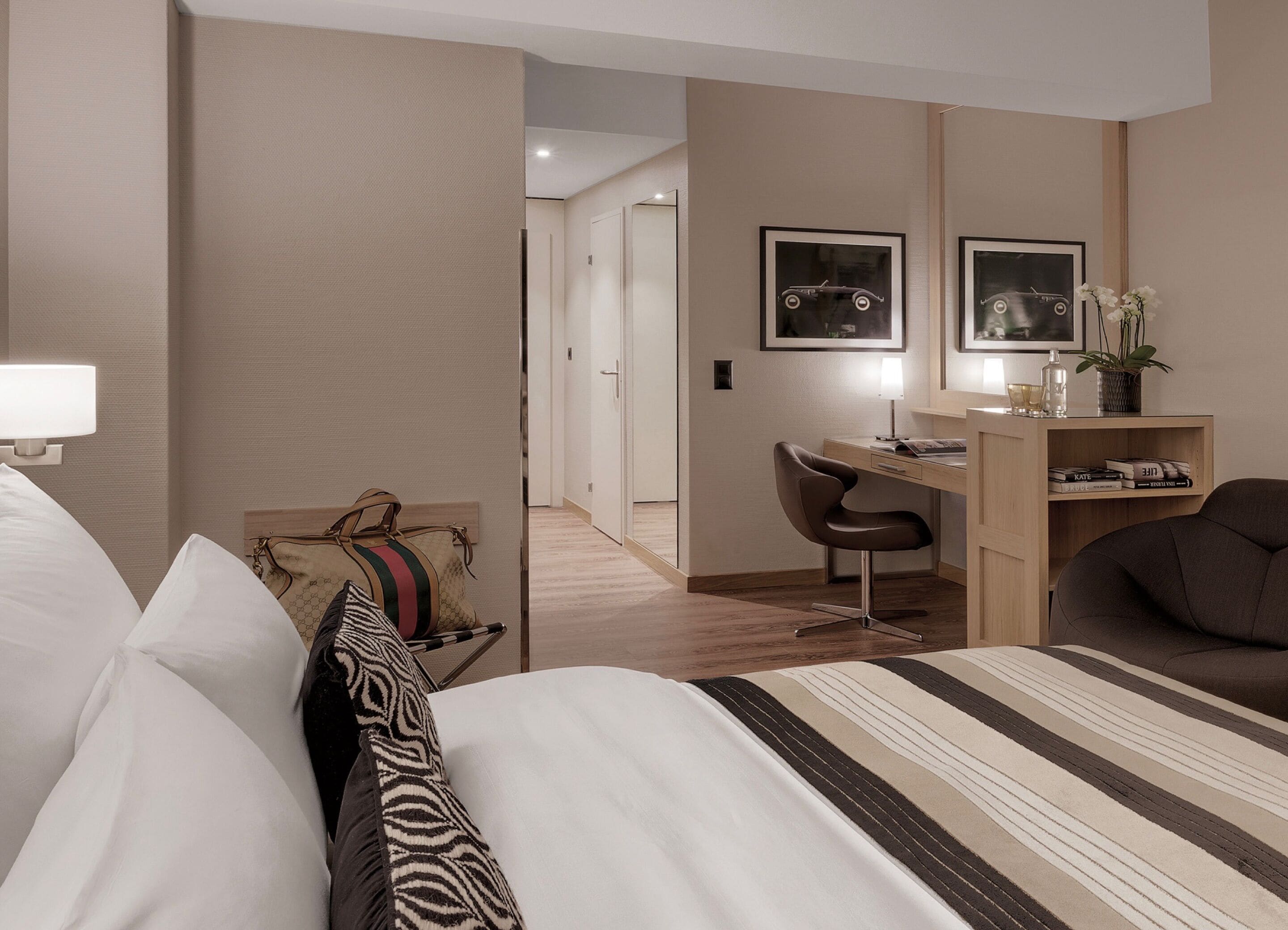 A hotel room with a bed, a desk, a chair, and a bookshelf.
